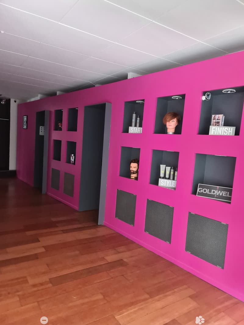 Interior of a beauty salon with a pink wall with several compartments, wooden floor, mannequin heads, and black speakers.