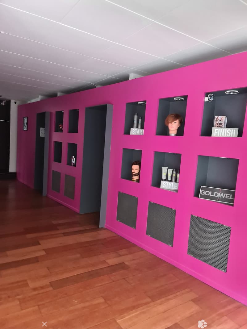 Interior of a beauty salon with a pink wall with several compartments, wooden floor, mannequin heads, and black speakers.