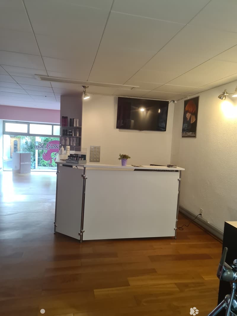 a white reception area with shelves, a monitor, and a potted plant. It has a tiled floor.