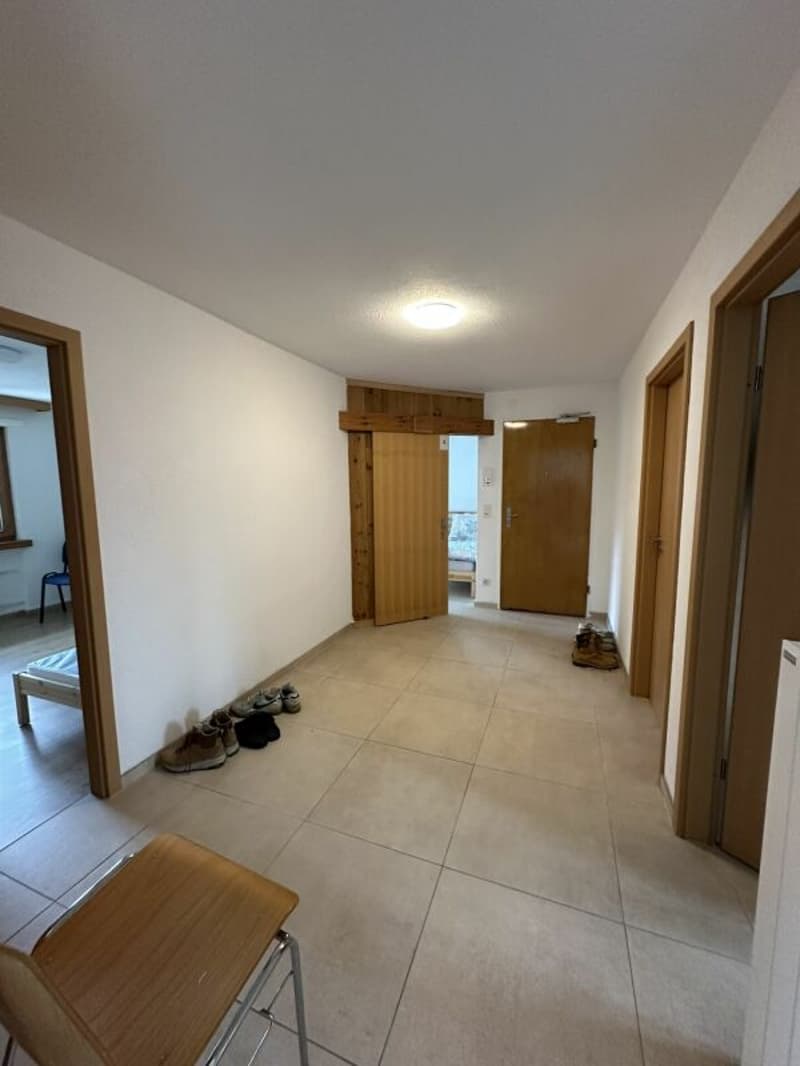 Empty hallway with tiled floor, wooden doors, and a chair