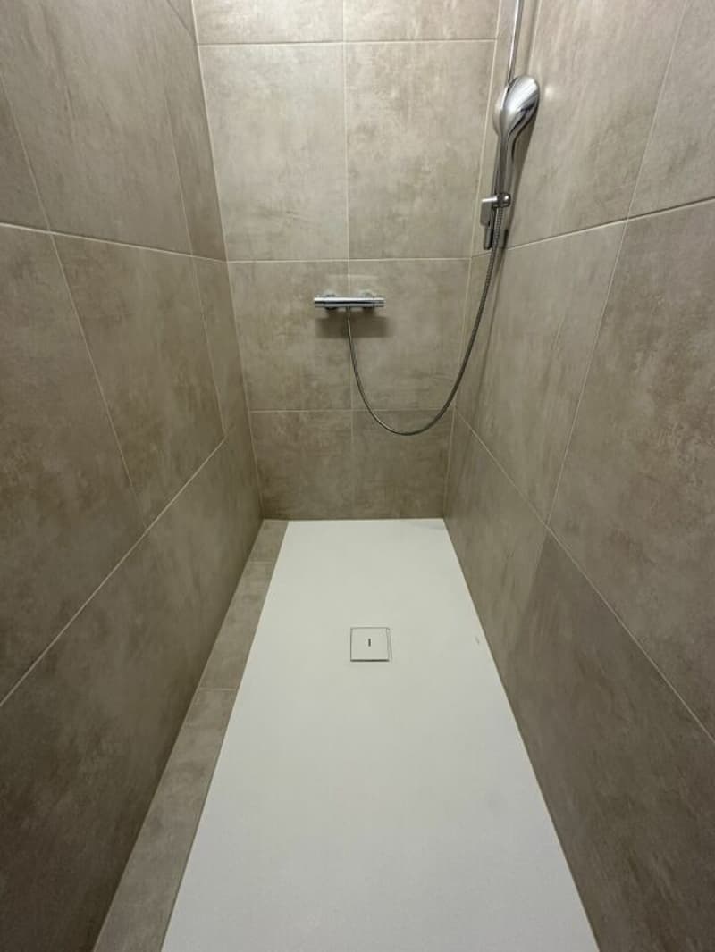 shower area with tiled walls, white floor, shower head and hose