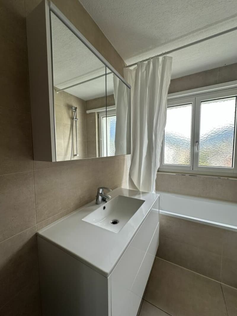 Bathroom with white sink, mirror, bathtub, and window with white curtain