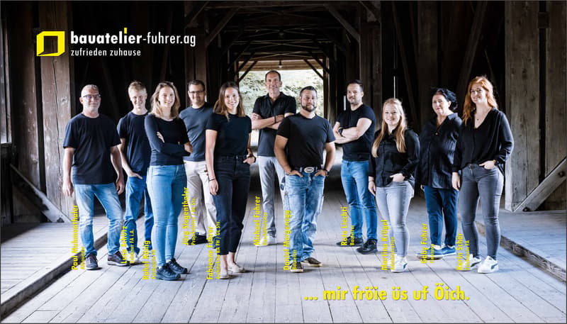 group of people dressed in black shirts and jeans standing in an arched area with wooden pillars, smiling