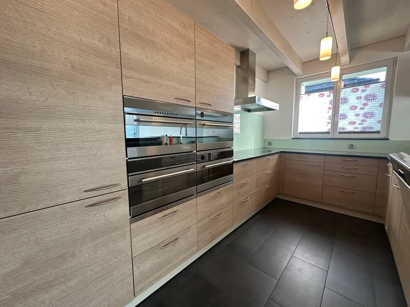 modern kitchen with wooden cabinets, stainless steel appliances, black tiled floor, large windows