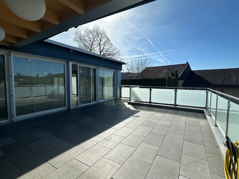 large balcony with glass railings, gray tiled floor, glass doors, view of the sky and trees