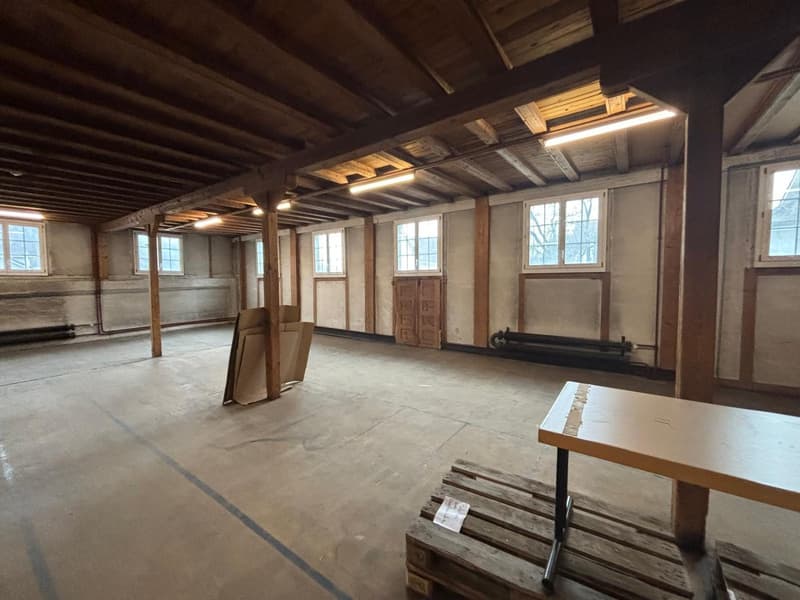 Large open room, wooden beams, concrete floor, multiple windows, wooden beams support ceiling
