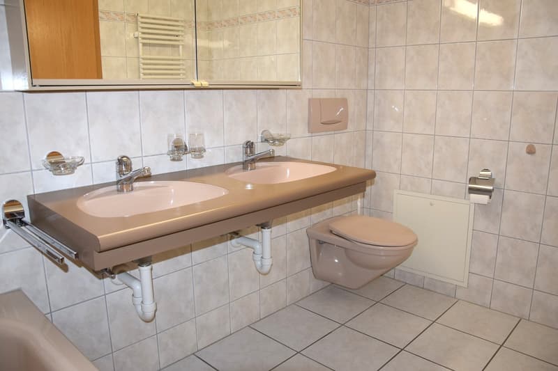 Bathroom with two sinks, toilet, bathtub, mirror, and tiled walls.