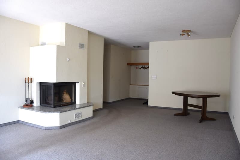 empty room with fireplace, wooden table, white walls, gray floor