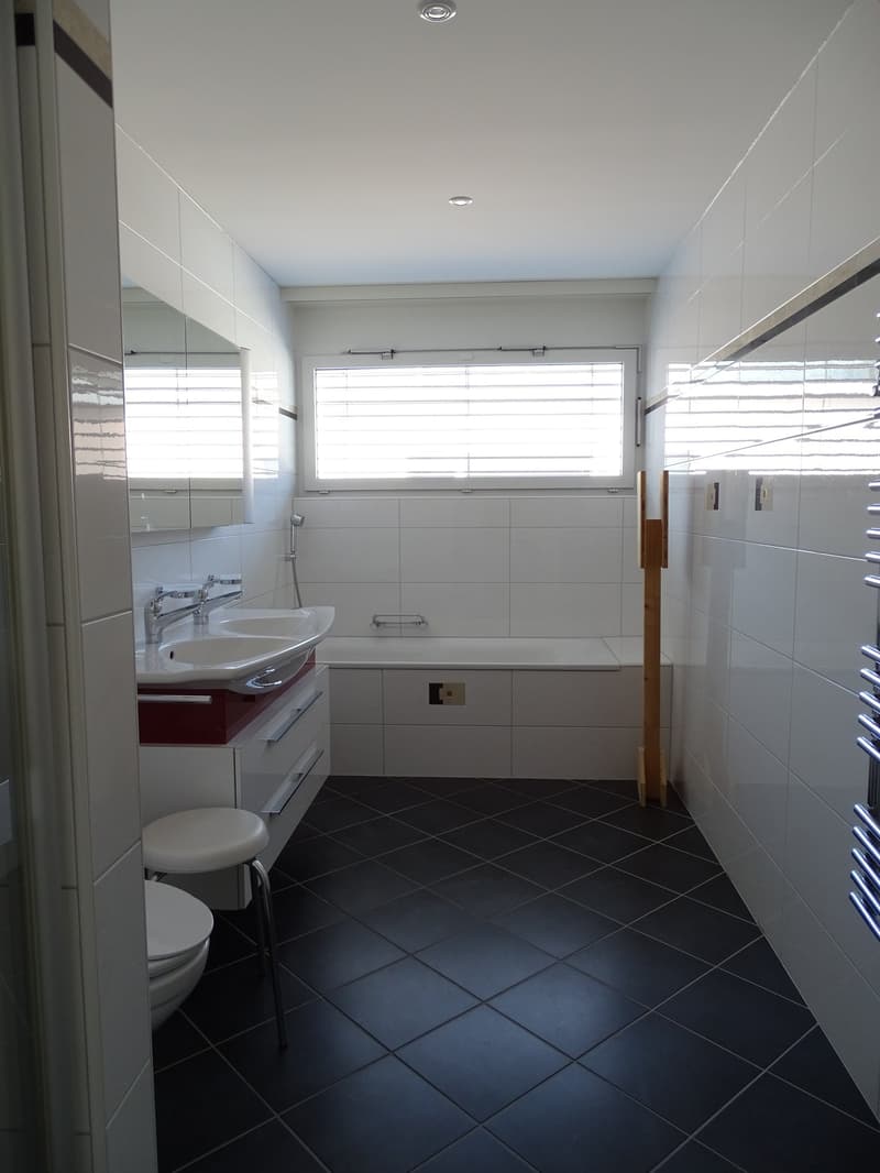 Modern bathroom with white tiles, double sink, bathtub, toilet, shower head, and towel rack