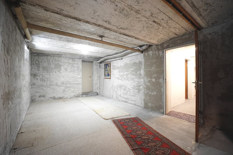 bare basement room with white walls, ceiling lights, carpet, open door, and pipe