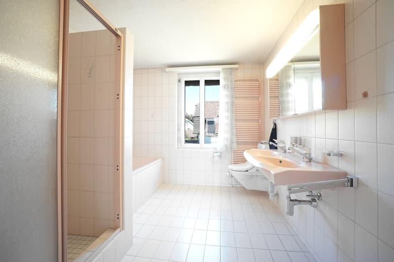 Bathroom with white tiles, bathtub, toilet, sink, mirror, radiator, and glass door.