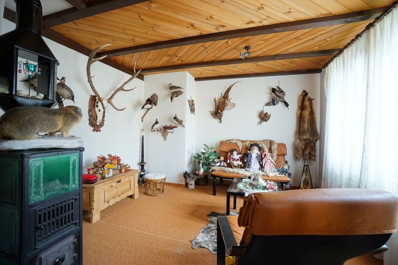 fireplace, brown couch, wooden chair, side table, wildlife trophies on wall, wooden beams ceiling