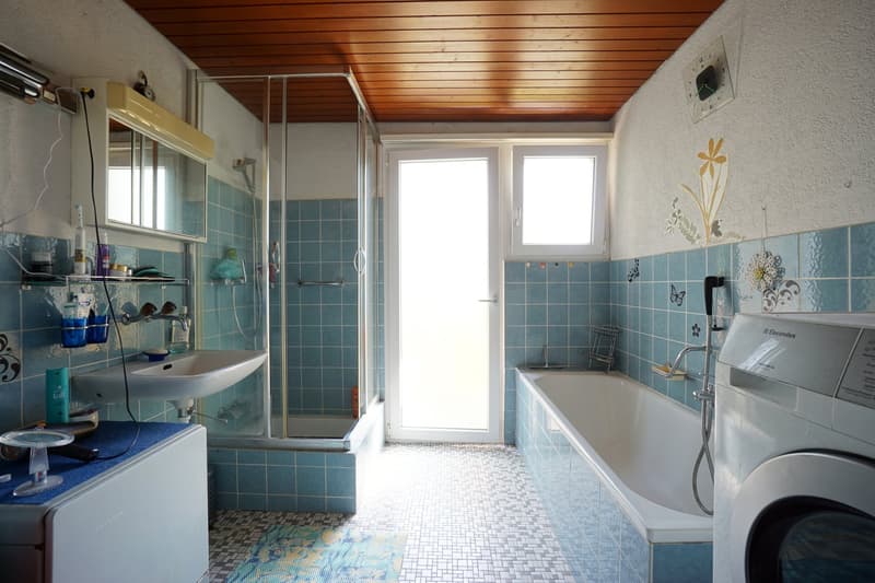 Blue tiled walls, white sink, glass enclosed shower, bathtub, wooden ceiling, washing machine