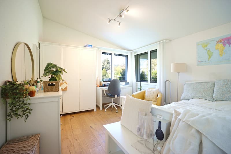 Bedroom with bed, desk, chair, cabinet, mirror, plants, lamp, world map, wooden floor