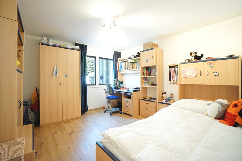 Bedroom with wooden floor, bed, desk, chair, shelves, and toys