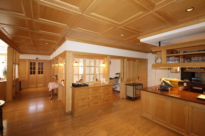 Large open-concept living space with wooden coffered ceiling, wooden cabinetry and furniture, tiled flooring, and a fireplace visible in the background.