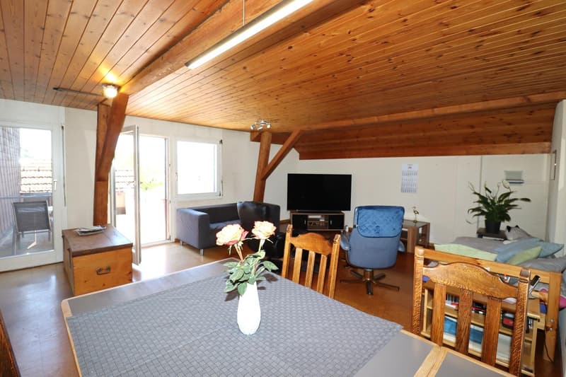 Spacious living room with wooden ceiling and walls, large windows, sofa, TV stand, desk, and a vase of flowers on the dining table