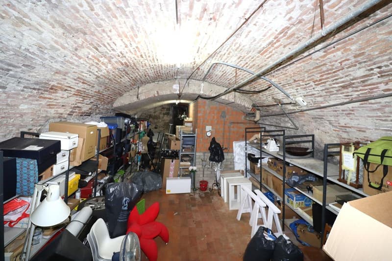 The image shows a cluttered storage room with various items such as boxes, furniture, and other household items stored in a brick-walled space with an arched ceiling.