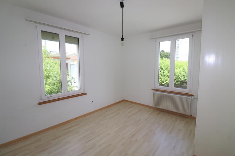 Empty room with wooden floors, white walls, two windows, and a radiator