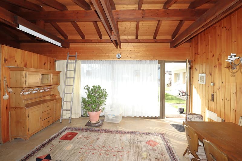 room with wooden walls, white curtains, wooden cabinet, ladder, potted plant, dining table, and chairs