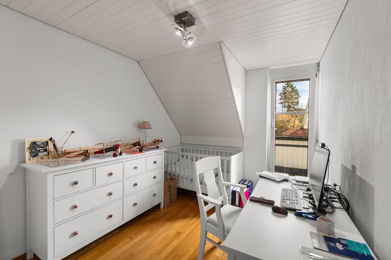 a white room with white ceiling, a desk with chair, a white dresser, a crib, and a monitor