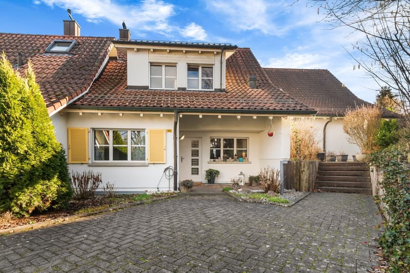 Detached 2-story house, red tiled roof, white walls, yellow shutters, a driveway, fenced front yard, several plants in front