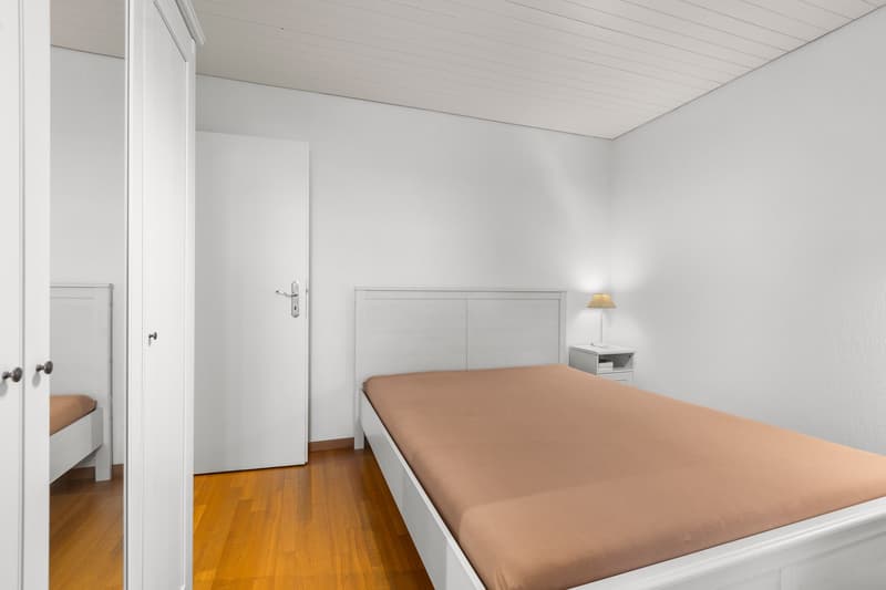 Single bed, side table with lamp, white doors, wooden floor
