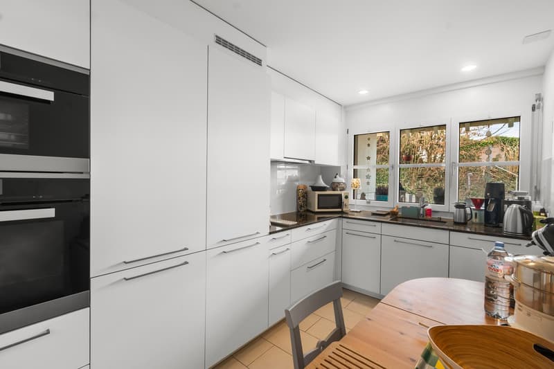 modern kitchen with white cabinetry, black oven, wooden table, tiled floor