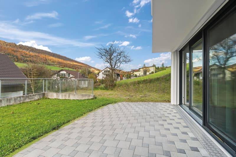 balcony with paved terrace, metal railing, glass doors, grassy hill in the background