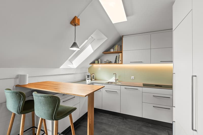 small kitchen with wooden table, white cabinets, green chairs, skylight, pendant light, sink, countertop, refrigerator