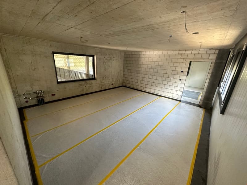 Unfinished concrete room with white tiled walls, concrete floor with yellow markings, and a window.