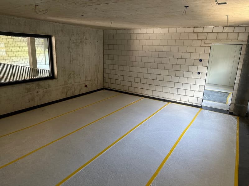 Unfinished room with concrete walls and floor, yellow striped markings on the floor, and a window
