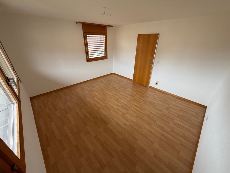 Empty room with wooden floors, white walls, two windows with shutters, wooden door