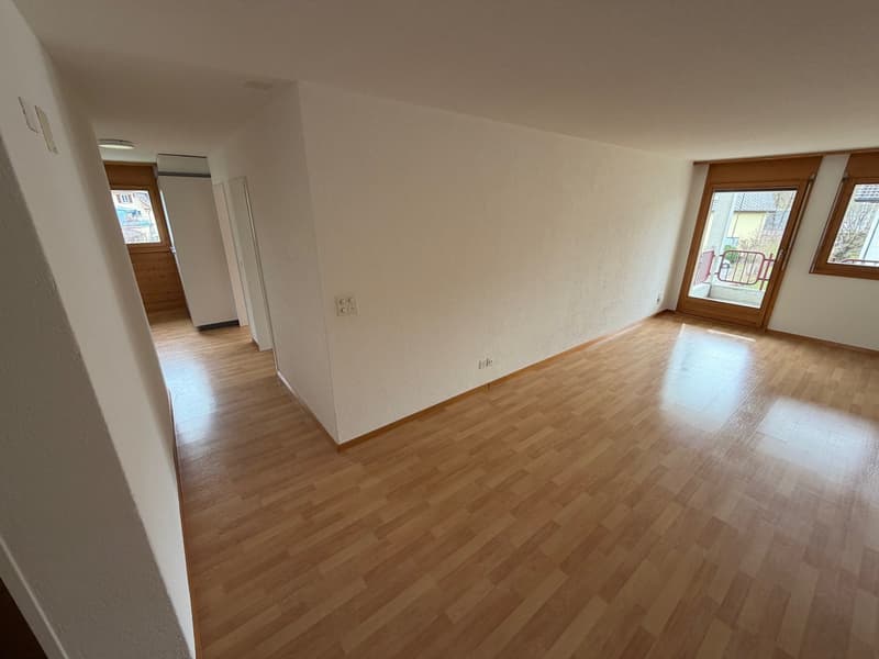 Large empty room, wood floor, white walls, two windows leading to a balcony, wooden doors