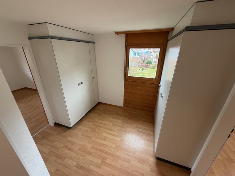 Wooden floor, white walls, large wardrobes, window with wooden frame