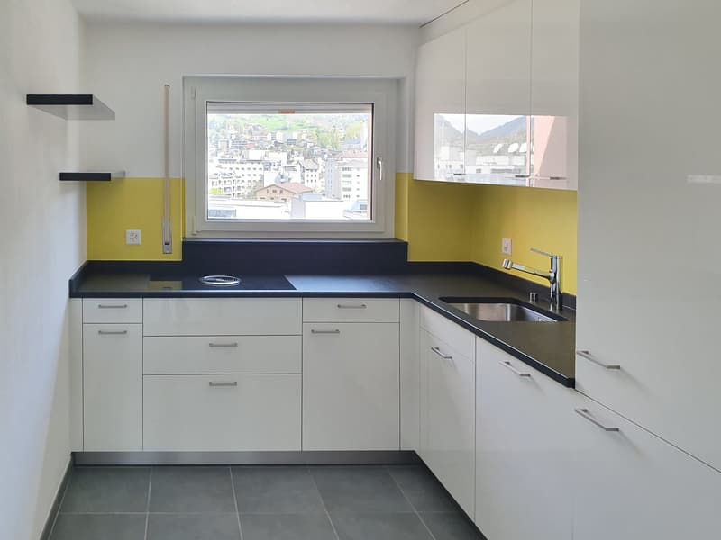 modern kitchen with white cabinets, black countertops, stainless steel sink, yellow accent wall, window with city view