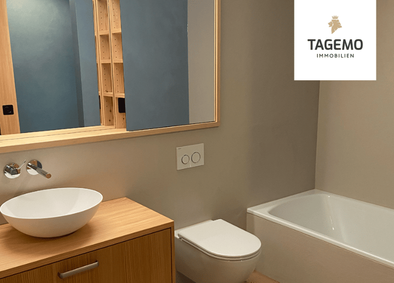 Bathroom with a wooden cabinet, a white sink, a mirror, a white bathtub, and a white toilet.