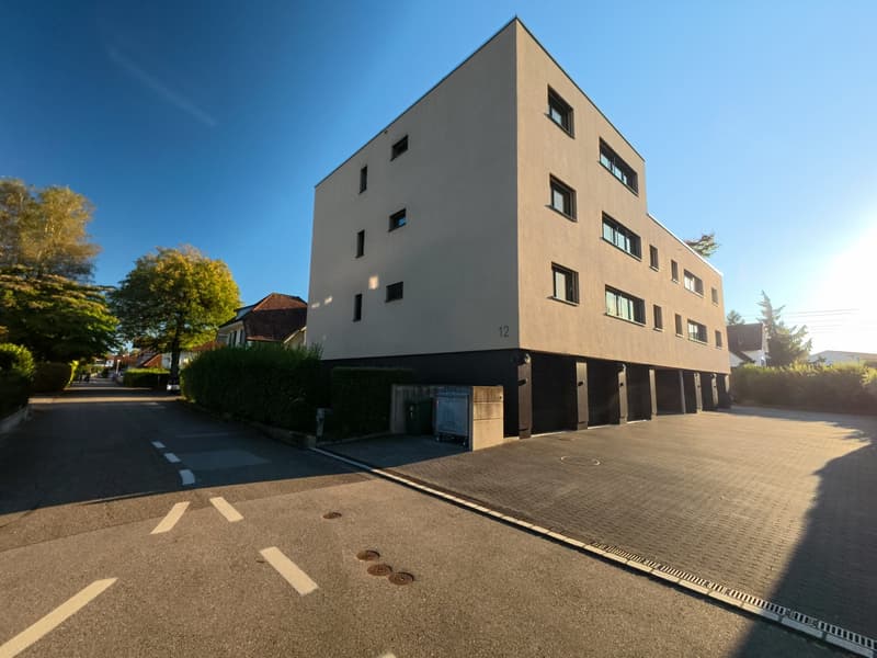 Modern apartment building with 4 floors, beige exterior, multiple windows, garage entrance at the bottom