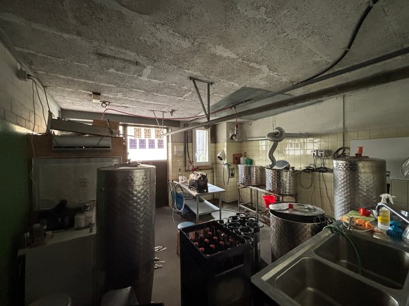industrial kitchen with large stainless steel tanks, metal tables, sink, and various kitchen equipment