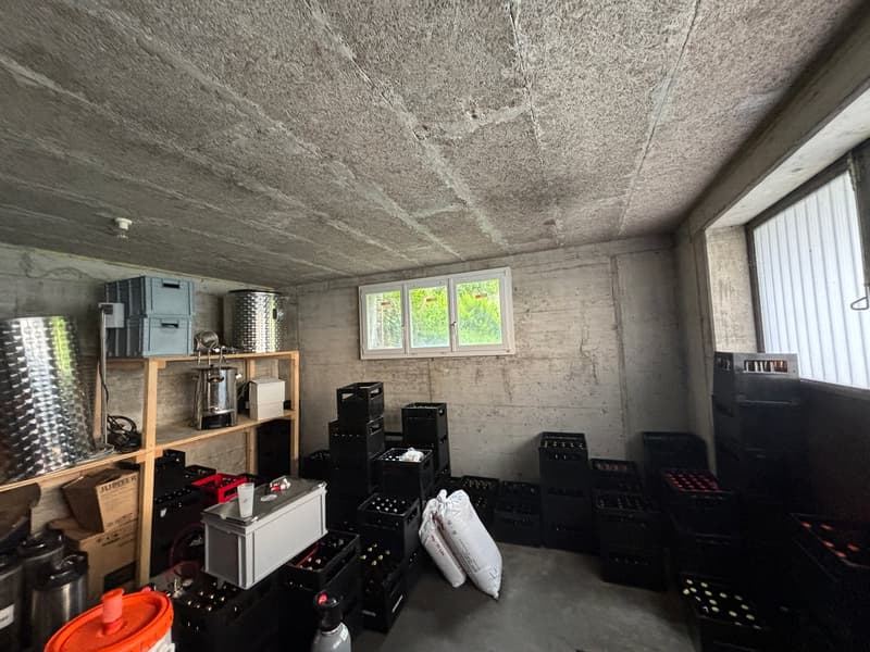 Storage room with concrete walls, wooden shelves, black crates, white sacks, metal containers, and a window.