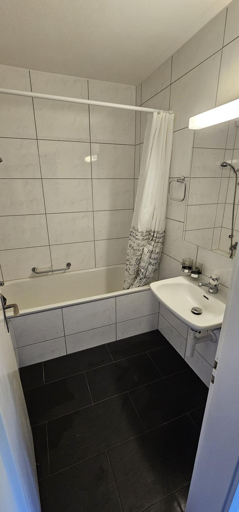 Bathroom with white tiles, bathtub, sink, shower curtain, and shower head.