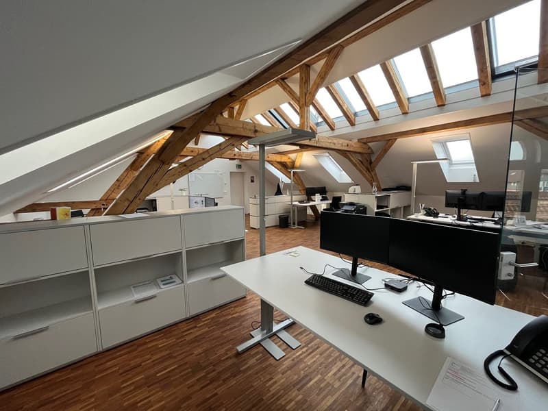 modern office space with wooden beams, white cabinets, desks, monitors, keyboards, telephones, and wooden floors