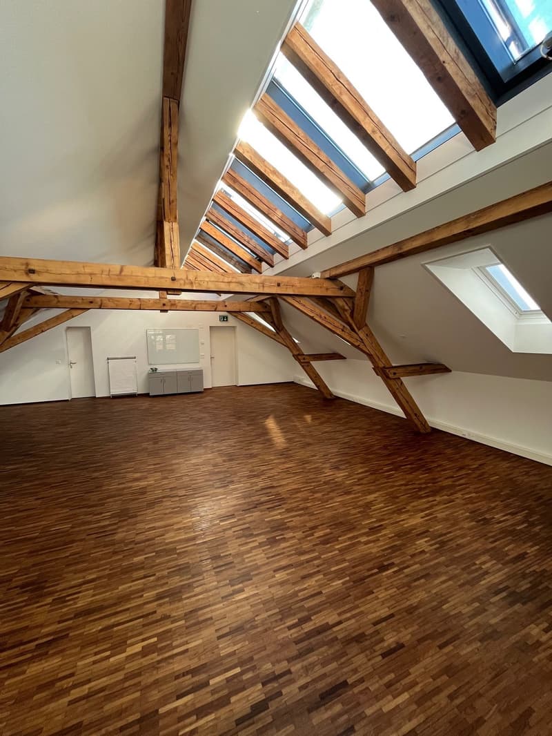 large room, wooden beams, wooden floor, white walls, skylights, two doors, small cabinet, whiteboard