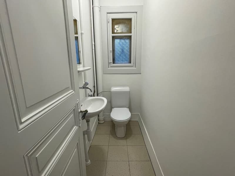 white sink, white toilet, small mirror, white floor tiles, white walls