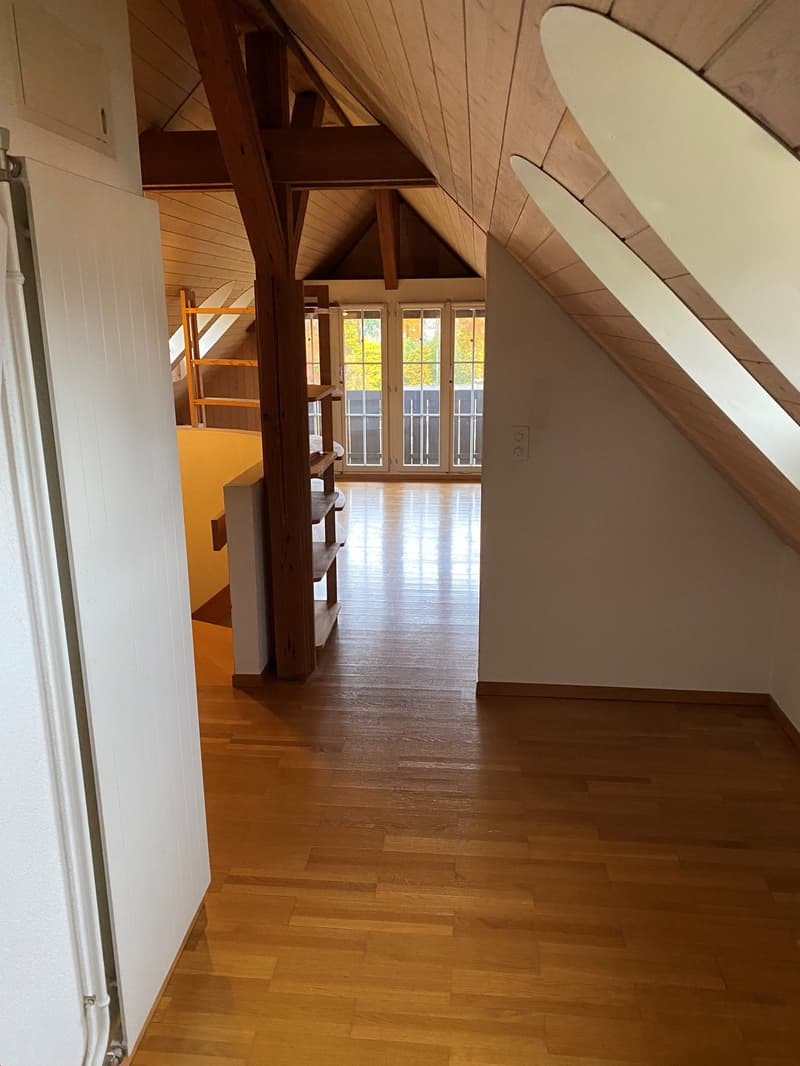 empty attic room, wooden floor, two sets of wooden beams, slanted ceiling, small shelves, two large windows