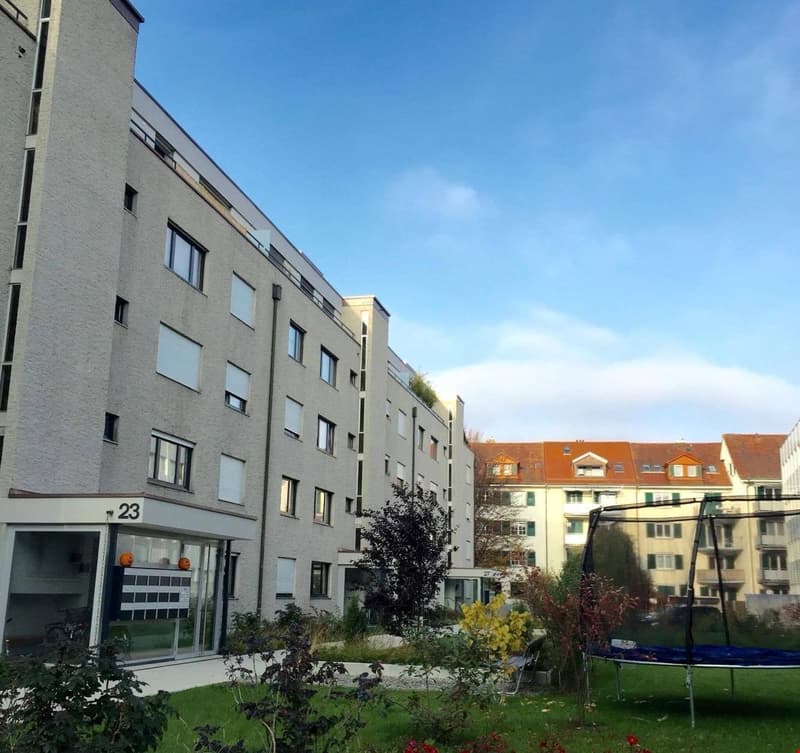 4 story building, balcony, garden with plants and grass, orange house in the background