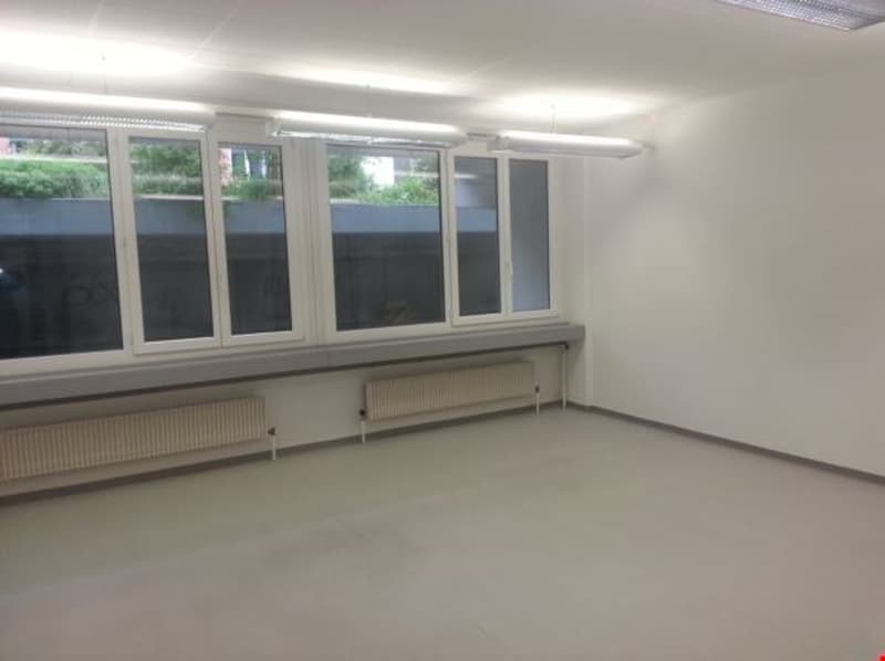 Empty room with large windows, white walls, white floor, built-in radiators beneath window sill, ceiling lights