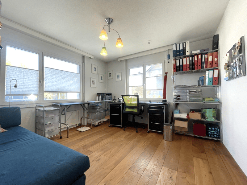 A room with a desk, chair, bed, shelves, and a lamp