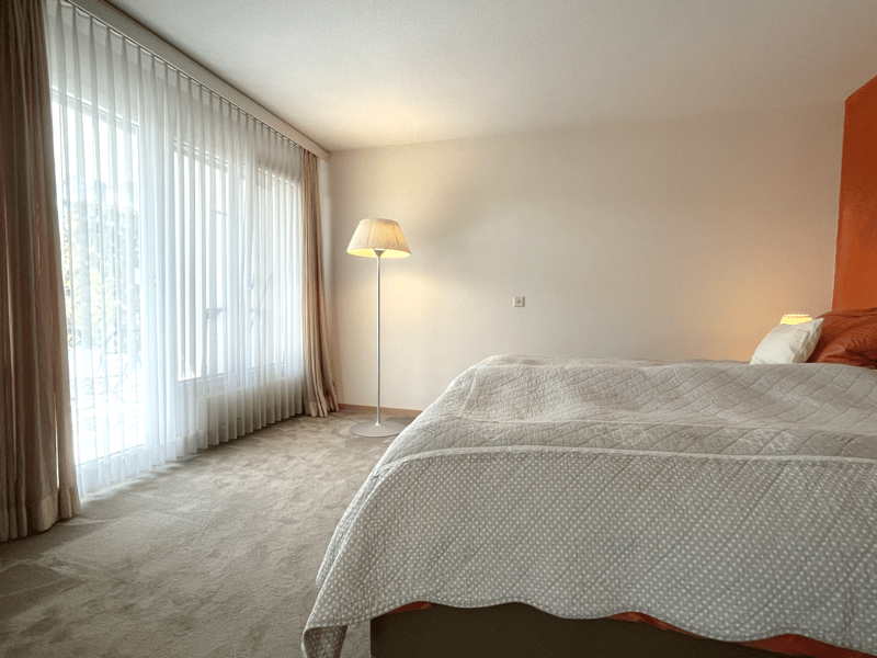 Bedroom with a bed, lamp, and large window with curtains