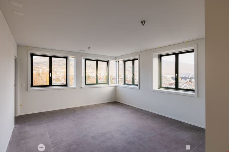 Empty room, 3 windows, white walls, gray floor, outside view of city